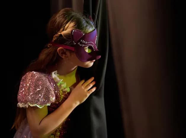 Child peeking behind stage curtain in drama class
